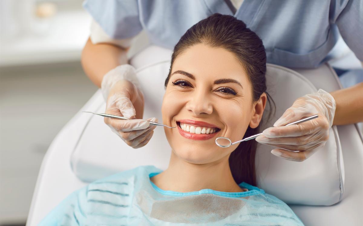 Una paciente sonríe en el sillón mientras el dentista sostiene el espejo y la sonda.